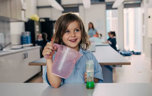 A child at school smiling and pouring something into a bottle