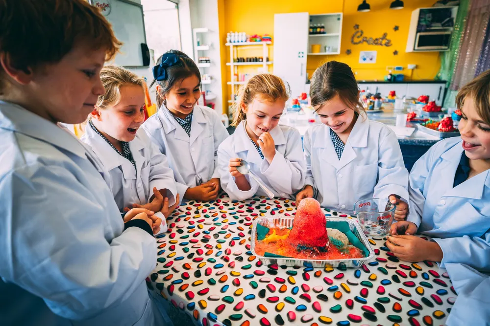 Kids in a lab coat gathered around smiling at a volcano exploding